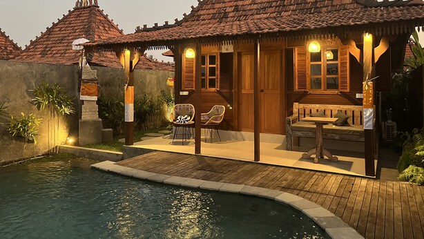 Una casa de madera tradicional con techo de tejas, piscina y mobiliario exterior.