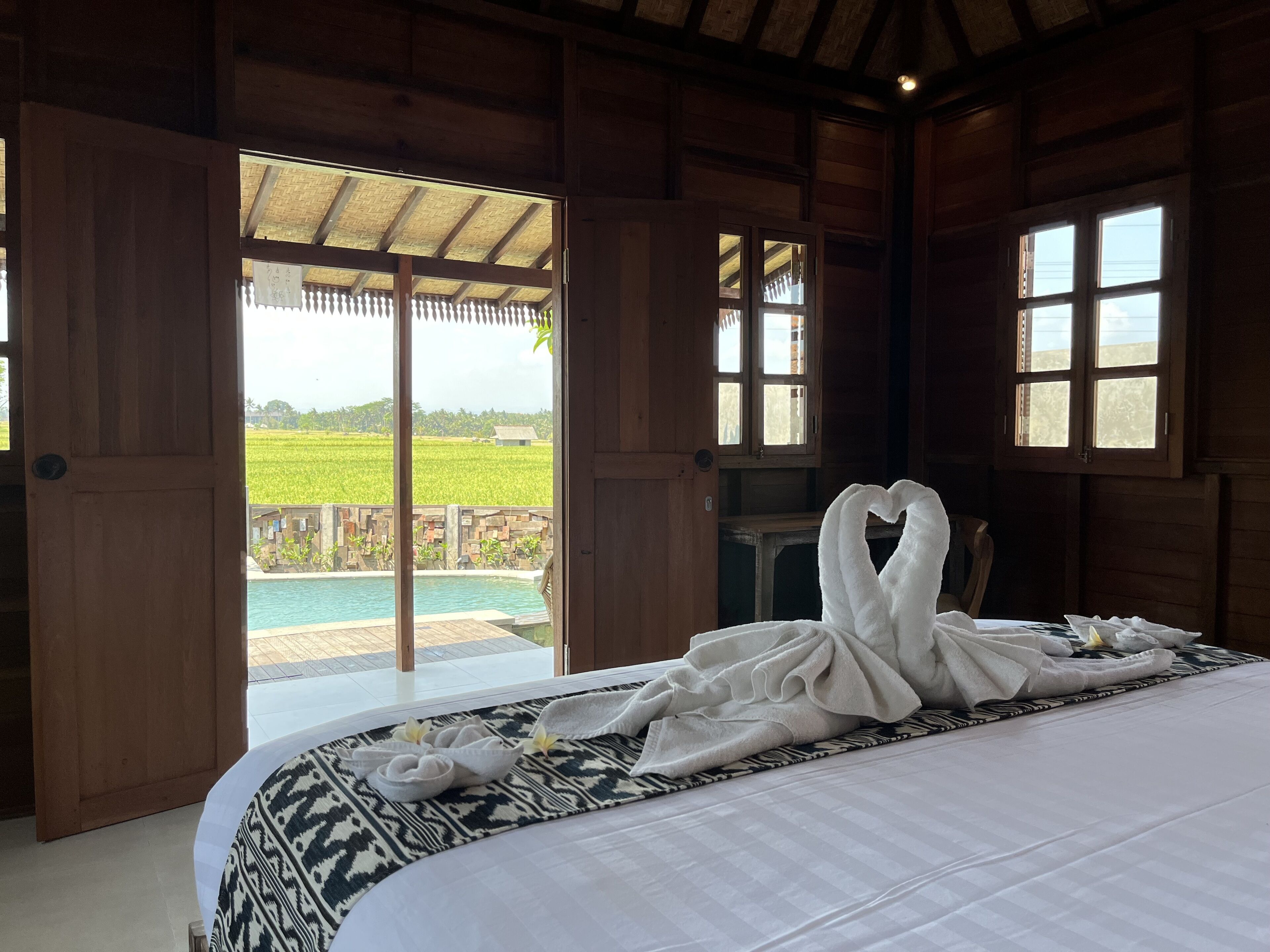 A bedroom with a large bed, a view of a swimming pool, and a wooden ceiling.