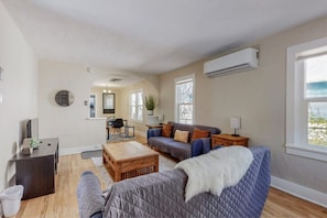 Ein geräumiges Wohnzimmer mit Sofa, Couchtisch und Fernseher. Im Hintergrund ist eine Essecke mit Tisch und Stühlen zu sehen.