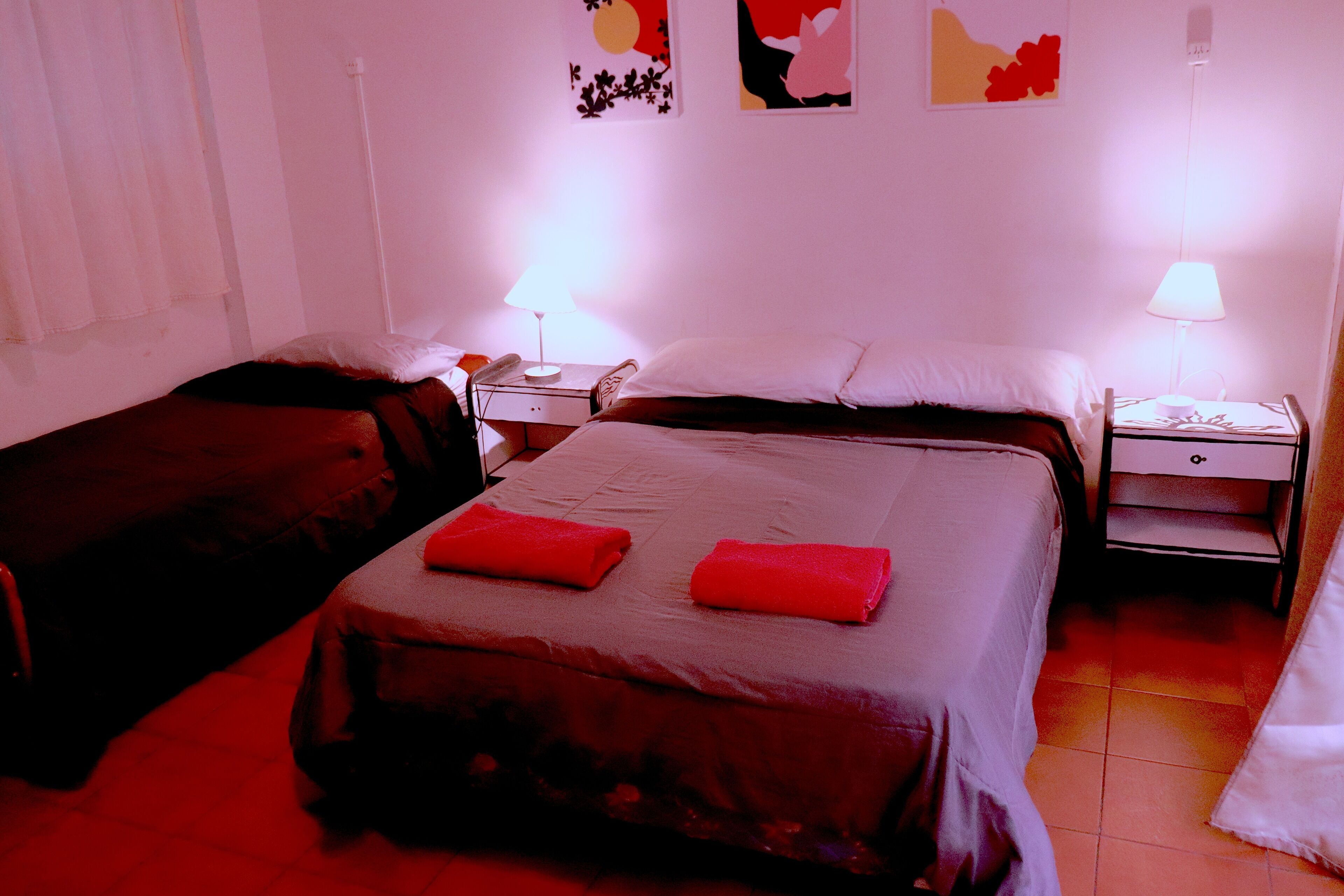 Habitación de hotel con dos camas, cada una con una toalla roja, una mesita de noche con lámpara y una pared decorada con arte abstracto.