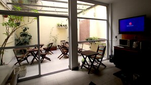 A room with a TV, a dining area with chairs and tables, and a view through large windows. - Ruda Hostel (Buenos Aires)