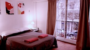 A hotel room with a bed, a nightstand, a window with curtains, and artwork on the wall. - Ruda Hostel (Buenos Aires)