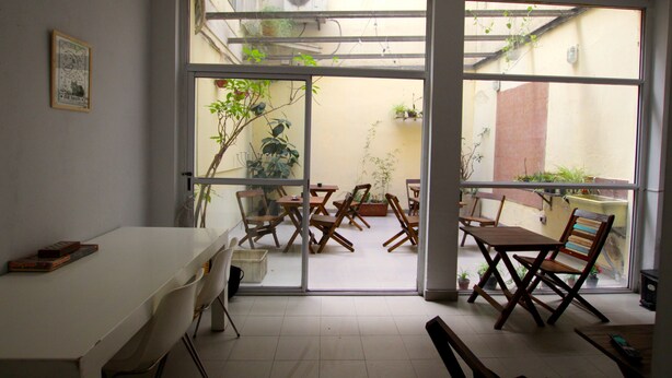 A room with a large sliding glass door leading to an outdoor patio area with wooden furniture and potted plants. - Ruda Hostel (Buenos Aires)
