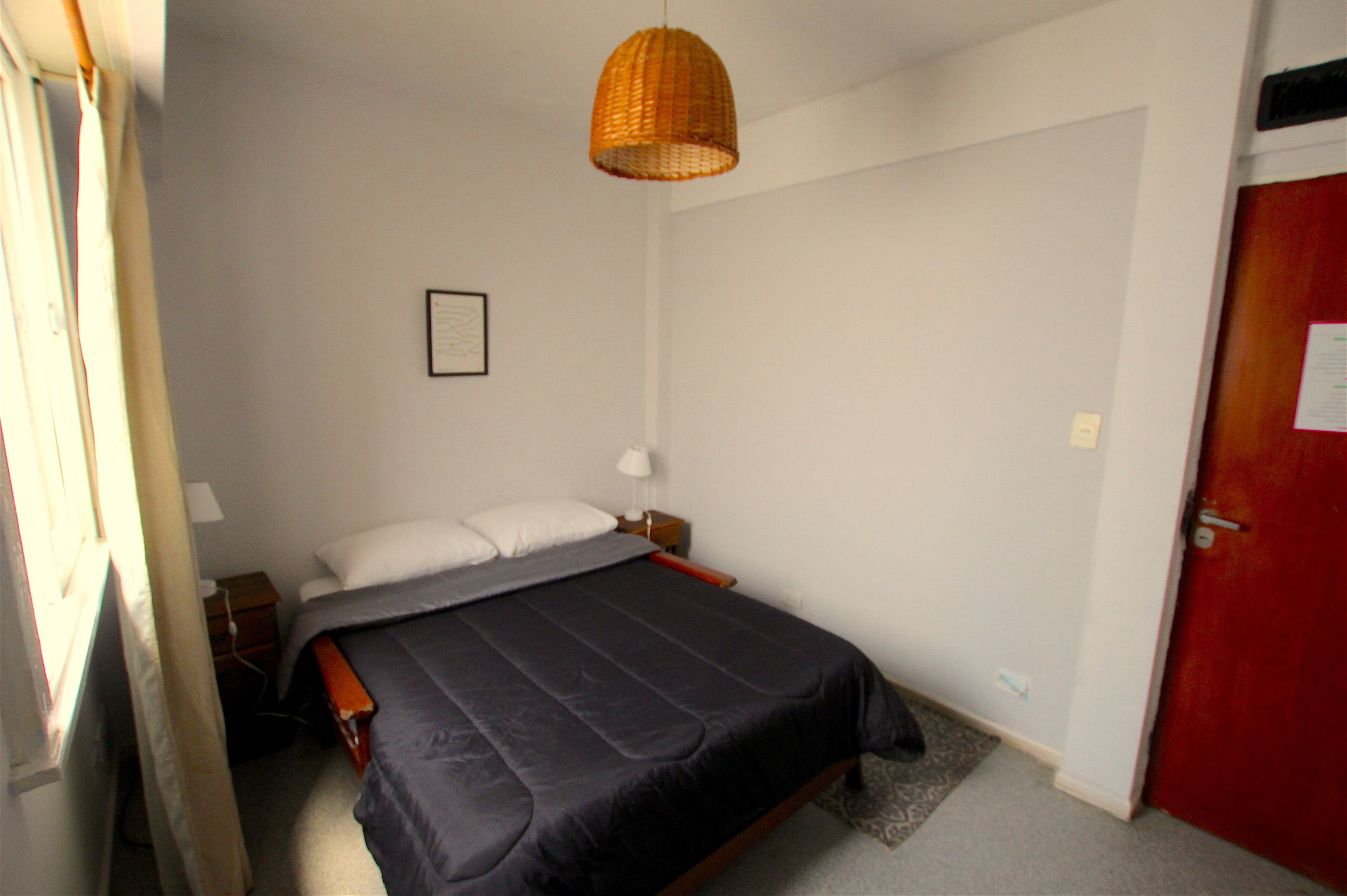 A bedroom with a single bed, a bedside table, a lamp, a hanging basket light, and a door with a notice.