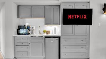 A modern kitchen with grey cabinetry, a built-in dishwasher, and a flat-screen TV mounted above the counter displaying the Netflix logo.