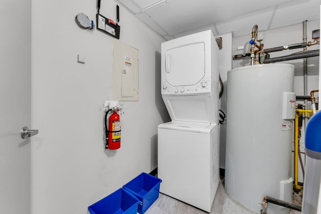 A laundry room with a white washing machine, a large water heater, and a fire extinguisher on the wall.