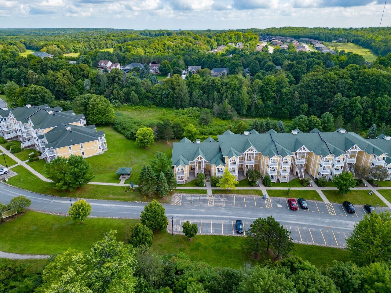 Una vista aerea di una zona residenziale con diversi edifici condominiali, un parcheggio e vegetazione circostante.