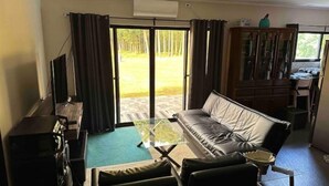 Un salon avec un canapé, une table basse et un téléviseur. Une porte-fenêtre coulissante donne accès à un patio.