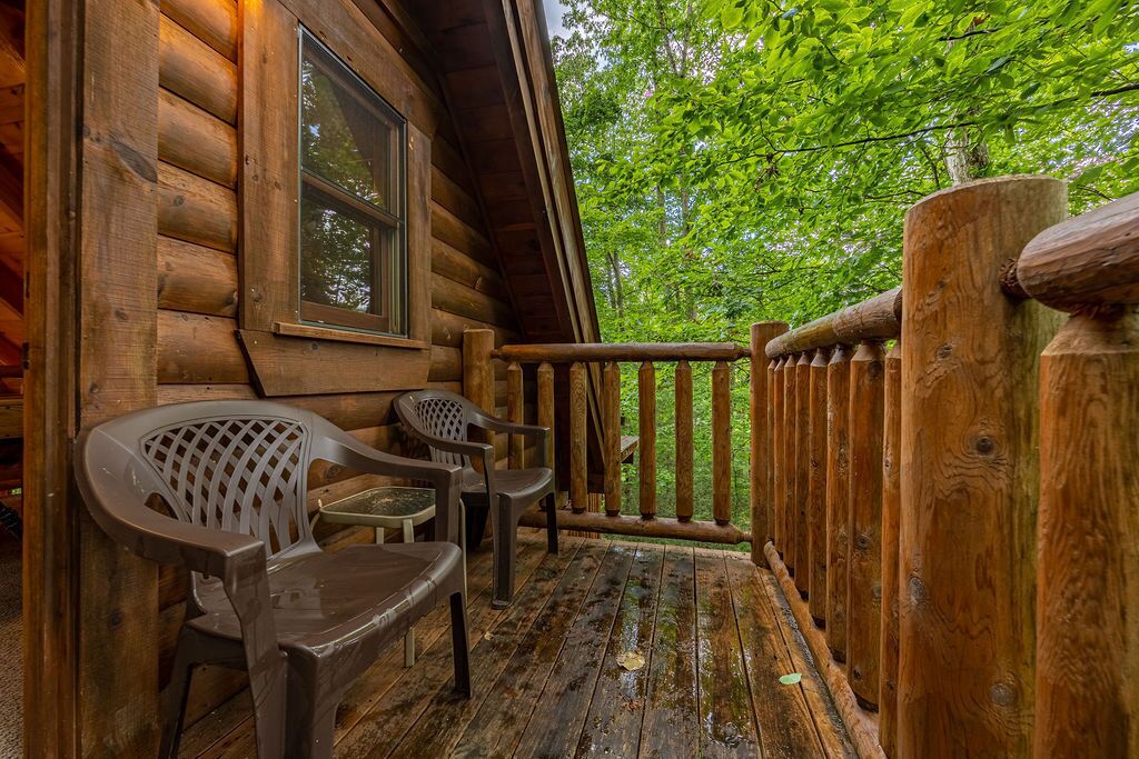 A wooden cabin with a porch, a window, and two plastic chairs.