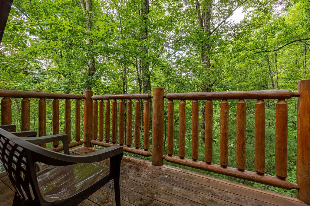 A wooden deck with a wooden railing, surrounded by lush green trees.