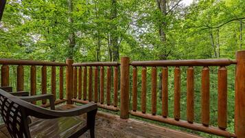 A wooden deck with a wooden railing, surrounded by lush green trees.