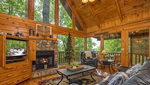A cozy cabin interior with a stone fireplace, leather sofa, and a television. - Happily Ever After (Gatlinburg)