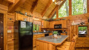 A cabin-style kitchen with wooden cabinetry, a black refrigerator, a microwave, and a wooden dining table with a bench. - Happily Ever After (Gatlinburg)