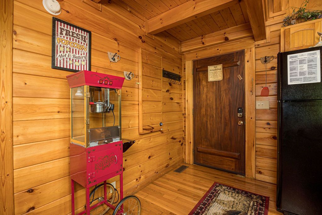 A wooden cabin interior with a popcorn machine, a door with a sign, and a refrigerator.