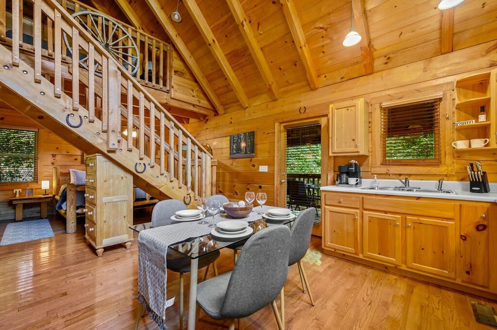 A wooden cabin with a dining area, kitchen, and a spiral staircase.