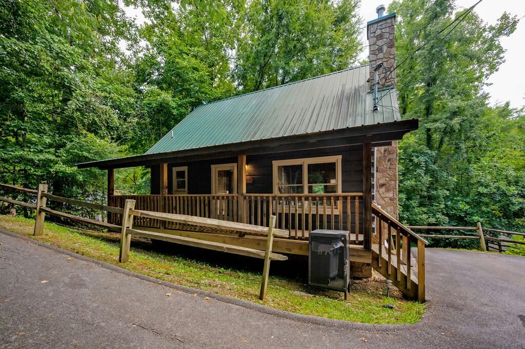A rustic cabin with a wooden deck, a stone chimney, and a metal roof.