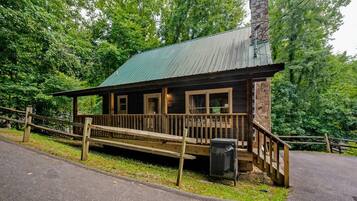 A rustic cabin with a wooden deck, a stone chimney, and a metal roof.