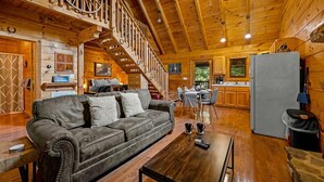 A wooden cabin interior with a sofa, dining table, kitchen, and a staircase with a wooden railing. - Sunrise Woods Retreat (Sevierville)