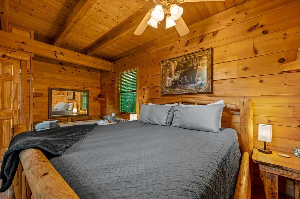 A wooden cabin bedroom with a bed, a mirror, a painting, and a ceiling fan.