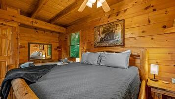A wooden cabin bedroom with a bed, a mirror, a painting, and a ceiling fan.
