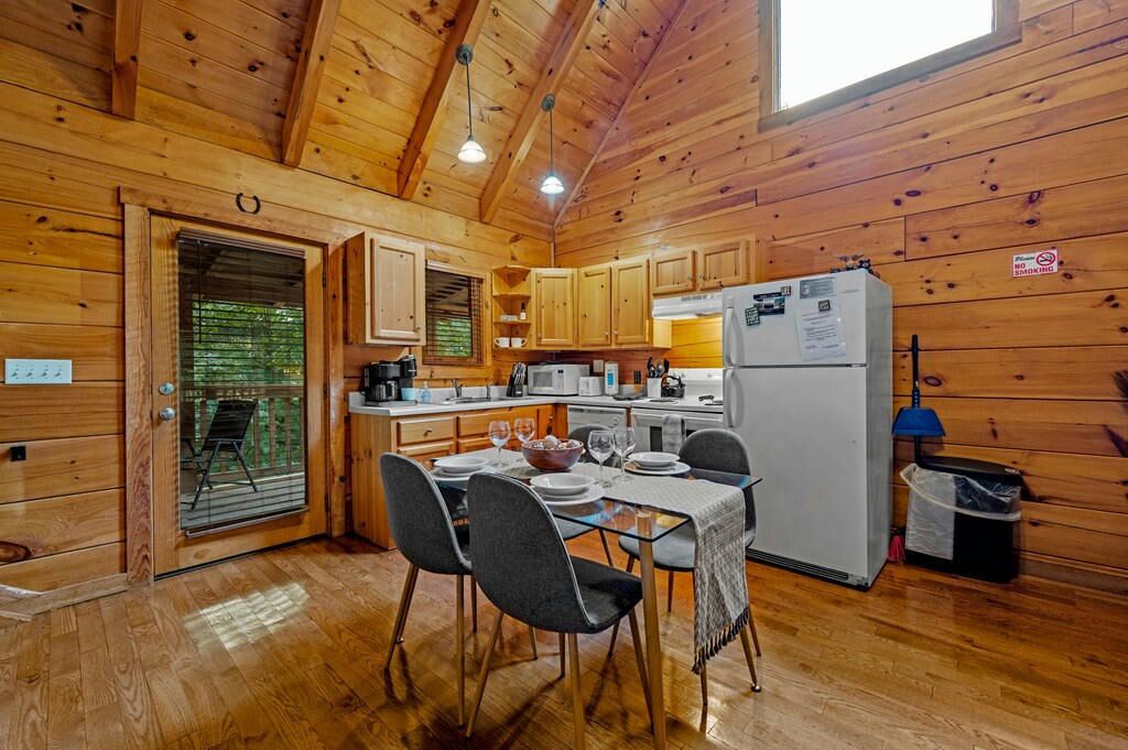 A wooden cabin interior with a dining area, kitchen, and a door leading outside.
