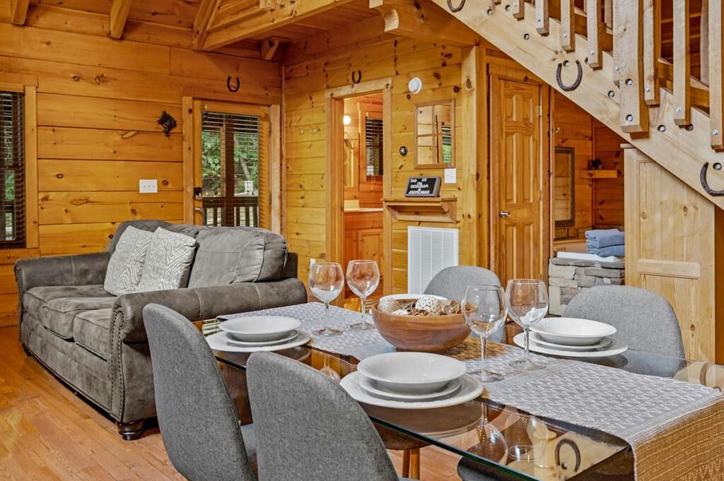 Ein Holzblockhaus-Innenraum mit Essbereich für vier Personen, einer Couch und einer Treppe.