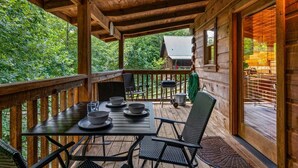 A wooden deck with a table set for dining, surrounded by chairs, and a view of the forest. - Sunrise Woods Retreat (Sevierville)