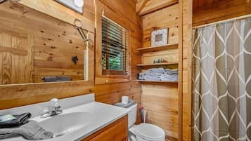 Baño de cabaña de madera con lavamanos, inodoro y cortina de ducha.