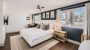 Ein Schlafzimmer mit Bett, Nachttischen, Deckenventilator und einem Fenster mit Vorhängen.