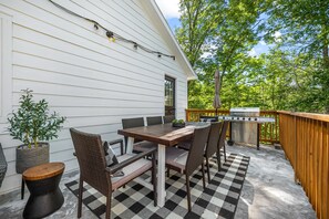 An outdoor patio with a wooden table and chairs, a grill, and a potted plant.