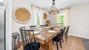 Comedor con mesa de madera dispuesta para seis personas, sillas negras y una araña.