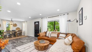 Una sala de estar moderna con un sofá marrón, una mesa de centro de madera y un ventanal con cortinas.