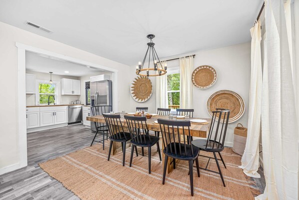 A spacious dining area with a large wooden table, black chairs, and a woven rug.