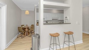 A modern kitchen with white cabinets, a stainless steel sink, and a built-in oven. There are two wooden stools and a trash can near the kitchen counter. - 4-min Walk to Ocean|2 King Suites|Beach Retreat (Myrtle Beach)