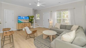 A modern living room with a sofa, coffee table, and bar stools. There is a TV, a plant, and a staircase leading to another room. - 4-min Walk to Ocean|2 King Suites|Beach Retreat (Myrtle Beach)