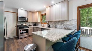A modern kitchen with white cabinets, a granite countertop, and a built-in island with bar stools. - 5BR|Private Lake|Pools|Hot Tub|Near Camelback (East Stroudsburg)