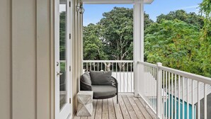 A covered porch with a white railing, a gray cushioned chair, and a view of a forested area. - Steps to Beach, Free Heated Pool & Fire Pit! (Panama City Beach)