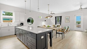 A modern kitchen with a large island, white cabinets, and a dining area with chairs and a table. - Steps to Beach, Free Heated Pool & Fire Pit! (Panama City Beach)