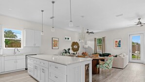 Une cuisine moderne avec des meubles blancs, un îlot central, des luminaires suspendus et un ventilateur de plafond.
