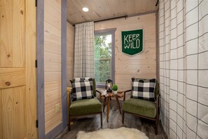 Ein gemütliches Cabin-Zimmer mit zwei gepolsterten grünen Sesseln, einem kleinen Tisch mit einer Laterne und einem Schild mit der Aufschrift 'KEEP IT WILD'.