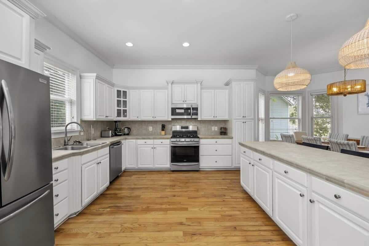 A spacious kitchen with white cabinetry, a stainless steel refrigerator, a built-in oven, and a large island with a sink.