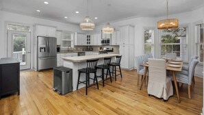 A spacious kitchen with white cabinetry, a central island, and a dining area with striped chairs. - Private Pool | Near MarshWalk & Beach | Fire Pit (Murrells Inlet)