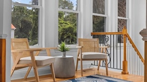 A room with large windows, a wooden staircase, and two wicker chairs with cushions. - Private Pool | Near MarshWalk & Beach | Fire Pit (Murrells Inlet)