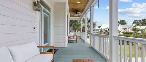 A covered porch with a wooden bench, a white sofa, and a table.