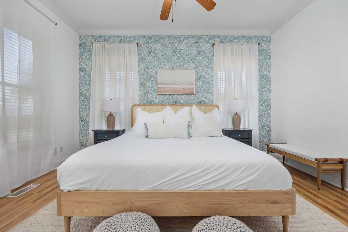 Un dormitorio con una cama de madera, ropa de cama blanca, dos mesitas de noche con lámparas y un cuadro colgado en la pared.