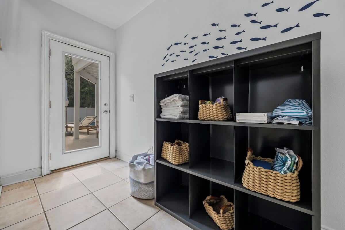 A hallway with a black shelving unit containing folded towels, baskets, and a door leading to a balcony.