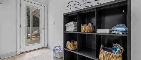 A hallway with a black shelving unit containing folded towels, baskets, and a door leading to a balcony.