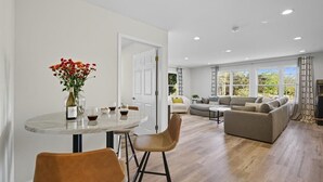 Ein modernes Wohnzimmer mit Essbereich, einer Sofagarnitur und einem großen Fenster, das natürliches Licht hereinlässt.