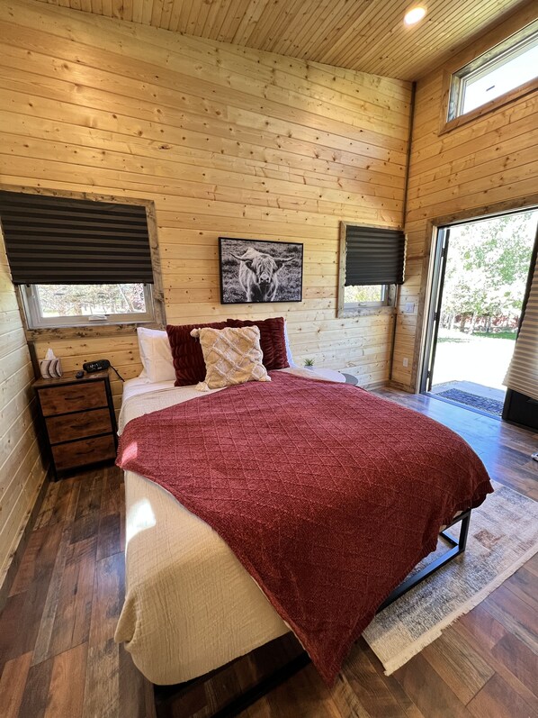 A wooden-paneled bedroom with a bed, nightstands, and a framed picture on the wall. - "The Matador" Westcliffe Outpost Cabin  (Westcliffe)