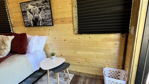 A cozy cabin room with a wooden ceiling, a bed with pillows, a small round table, a potted plant, and a window with blinds. - "The Matador" Westcliffe Outpost Cabin  (Westcliffe)